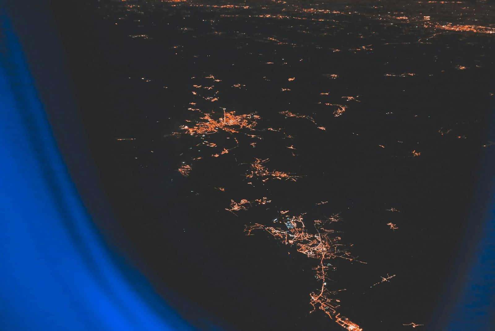 Orange town lights scattered across dark ground at night, seen past the blue-lit edge of an aircraft window