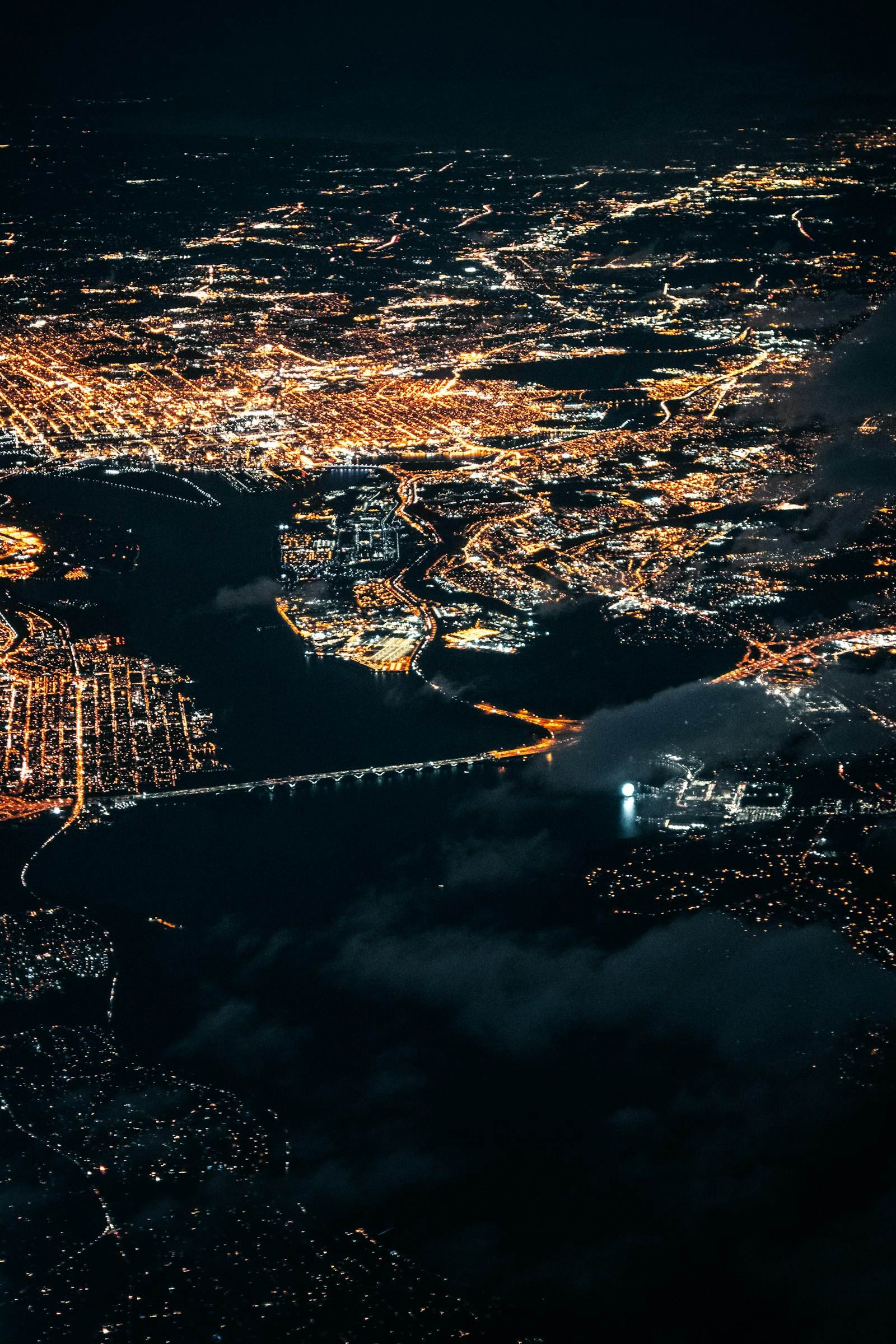 A city at night seen from an aircraft, with a lit bridge over dark water