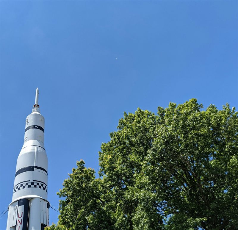 The Saturn V rocket replica rising above trees against a blue sky